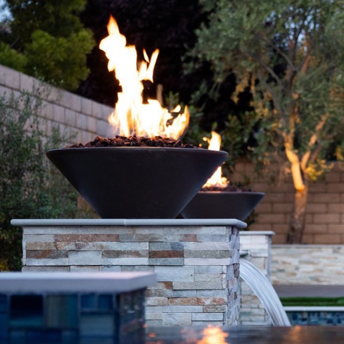 The Outdoor Plus Cazo Concrete Fire Bowl in a garden setting