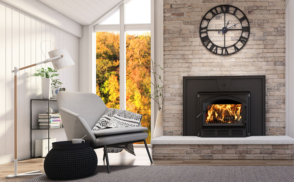 Enerzone Solution 3.5 wood insert with a fire burning, installed in a light brick fireplace in a living room with an armchair and autumn view through the window