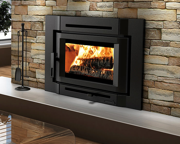 Enerzone Destination 2.3-I wood insert with a fire burning, shown wide in a stone fireplace with its contemporary flush cast iron surround and fireplace tools alongside